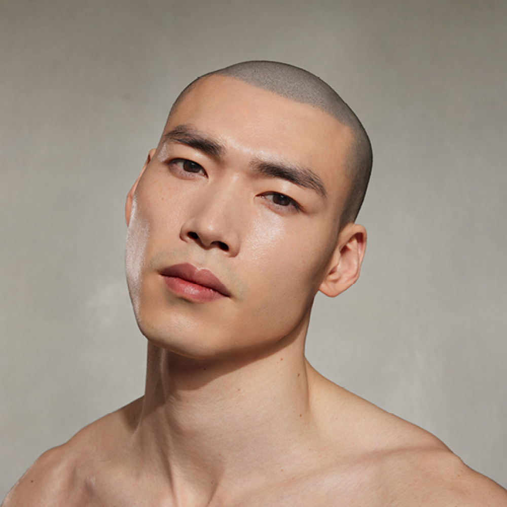 Mann mit nackten Schultern blickt leicht geneigt vor grauem Hintergrund.