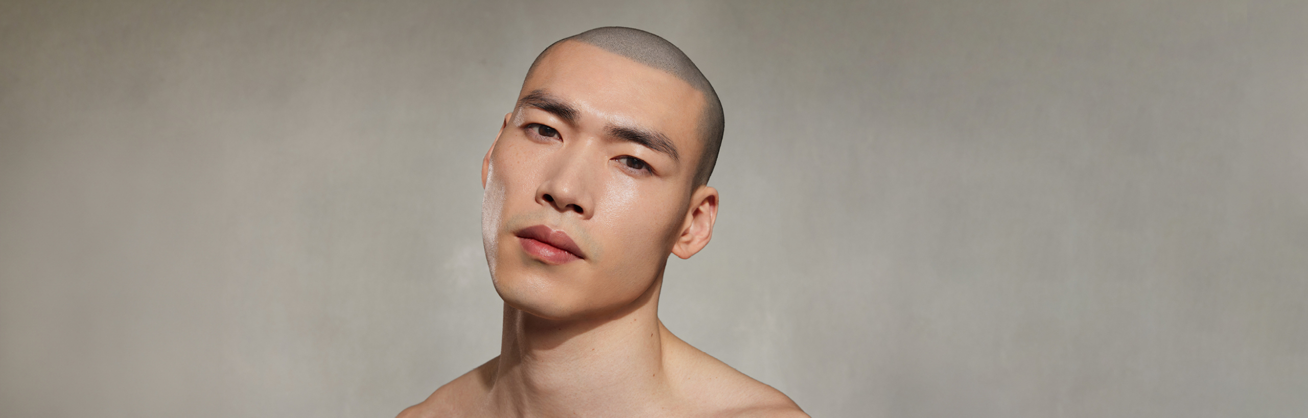 Mann mit nackten Schultern blickt leicht geneigt vor grauem Hintergrund.