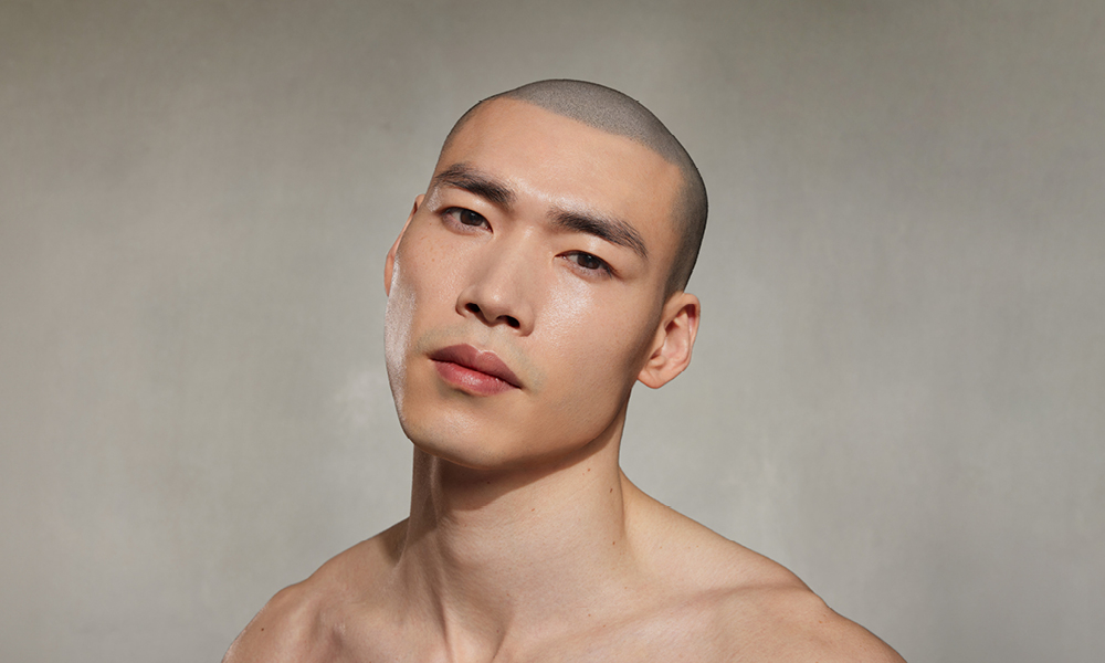 Mann mit nackten Schultern blickt leicht geneigt vor grauem Hintergrund.